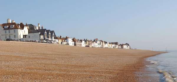 Deal seafront showing pebble beach and cottagers on the sky line.