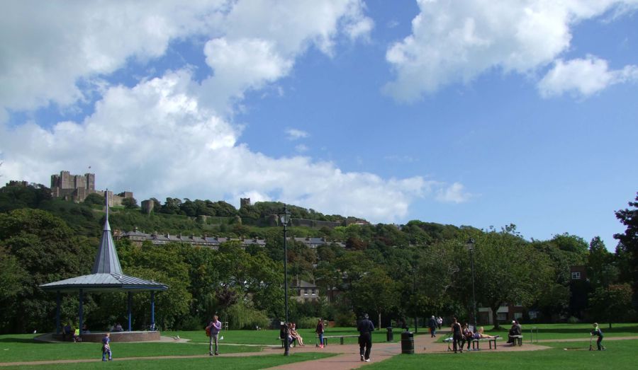 People strolling through a public park with a bandstand and castle in the background.