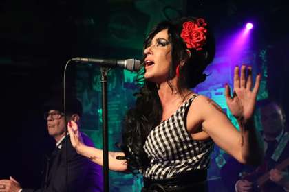 Photo of Caroline Lowe as Amy Winehouse on stage with a microphone