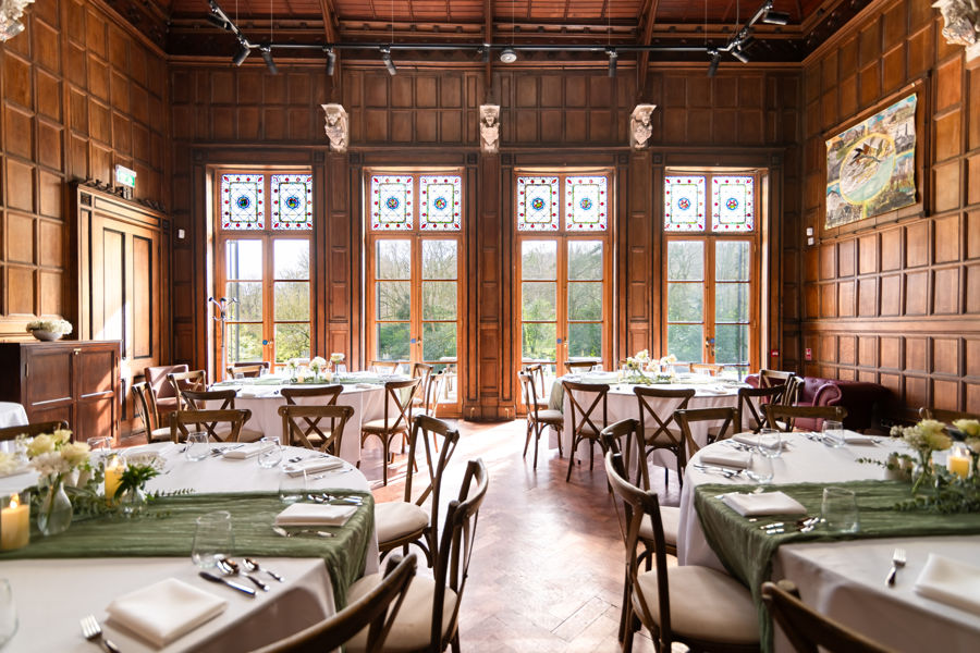 A wood-panelled room with round tables and chairs laid for a wedding reception.