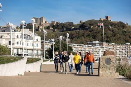 A group of people walking on Dover seafront with the castle in the distance