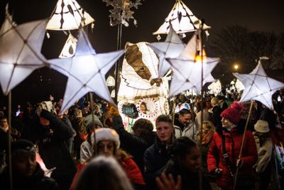 A crowd of people holding lanterns on sticks in the dark.