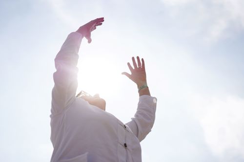 A person with their arms raised towards the sun.