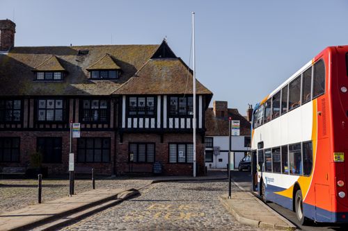 A red, yellow, blue and white Stagecoach bus at a bus stop outside Sandwich Guildhall.