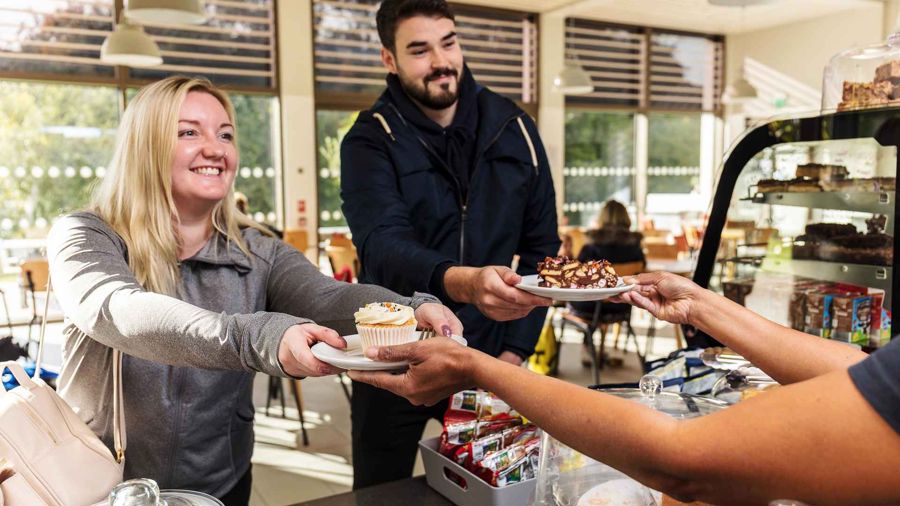 A man and a woman being handed cakes on two plates in a cafe surrounding.