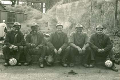 Black and white image of miners sitting in a fow