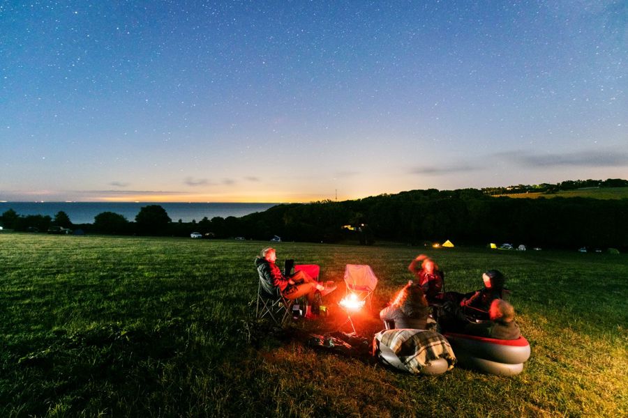 A family sitting round a campfire on a campsite with the sea in the background