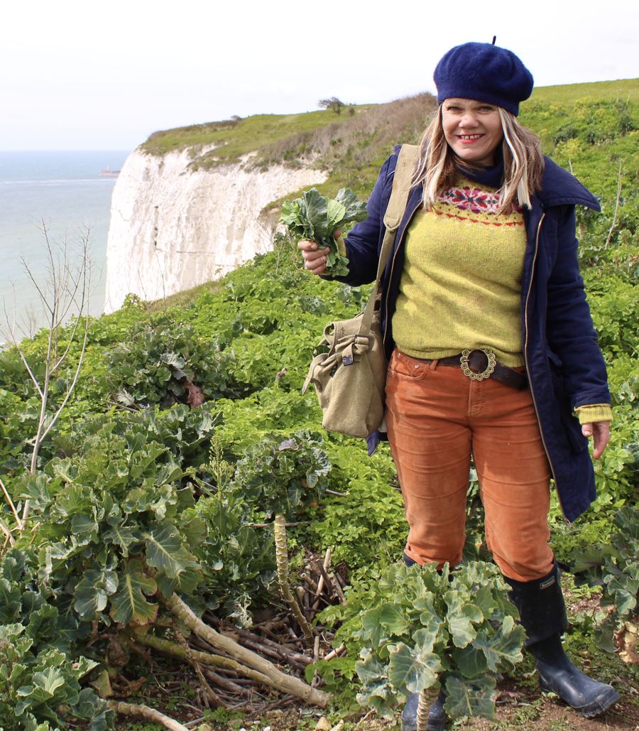 A woman standing on a cliff holding a bunch of sea kale.