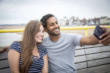 A woman wearing a striped t-shirt and a man wearing a grey t-shirt smiling taking a selfie