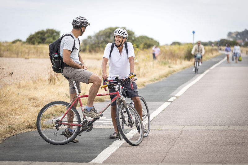 Two cyclists having a chat on a marked cycle path with others in the background.