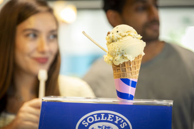 Ice cream in a cone with two people standing behind.