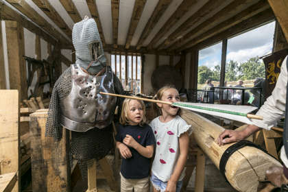Two children smiling at someone off camera. A wooden arrow embedded in a suit of armour.
