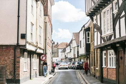 A street of medieval buildings in Sandwich a few people and cars in the distance.