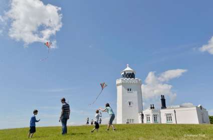 A family flying kites in front of a whitewashed lighthouse