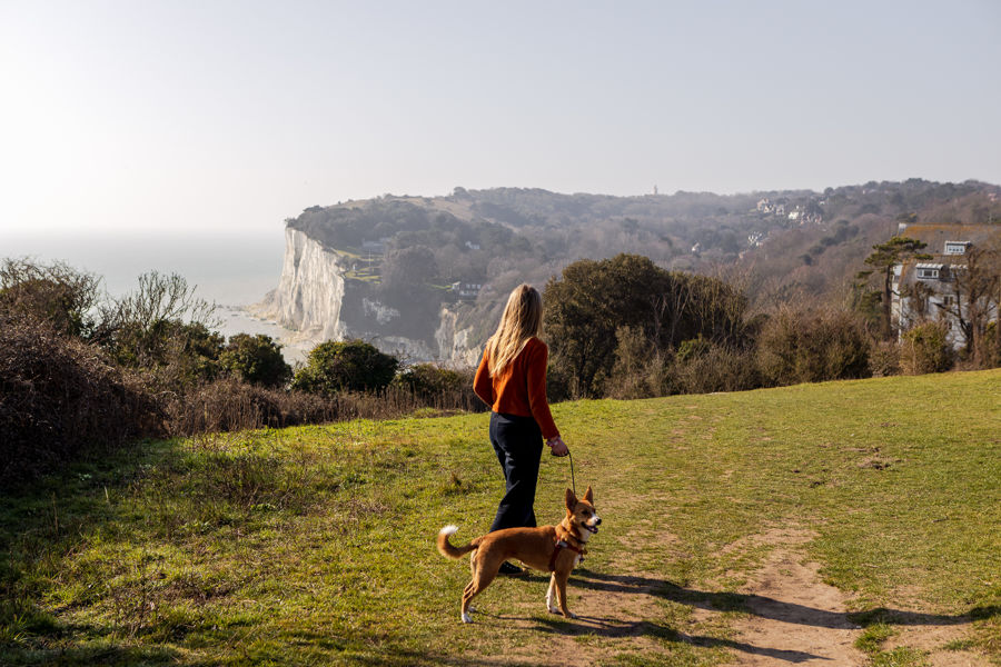 A woman walking a dog with the sea and white cliffs in the background