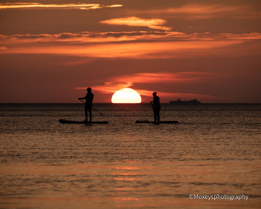 Two paddleboarders' silhouettes on the sea with setting sun in the background.